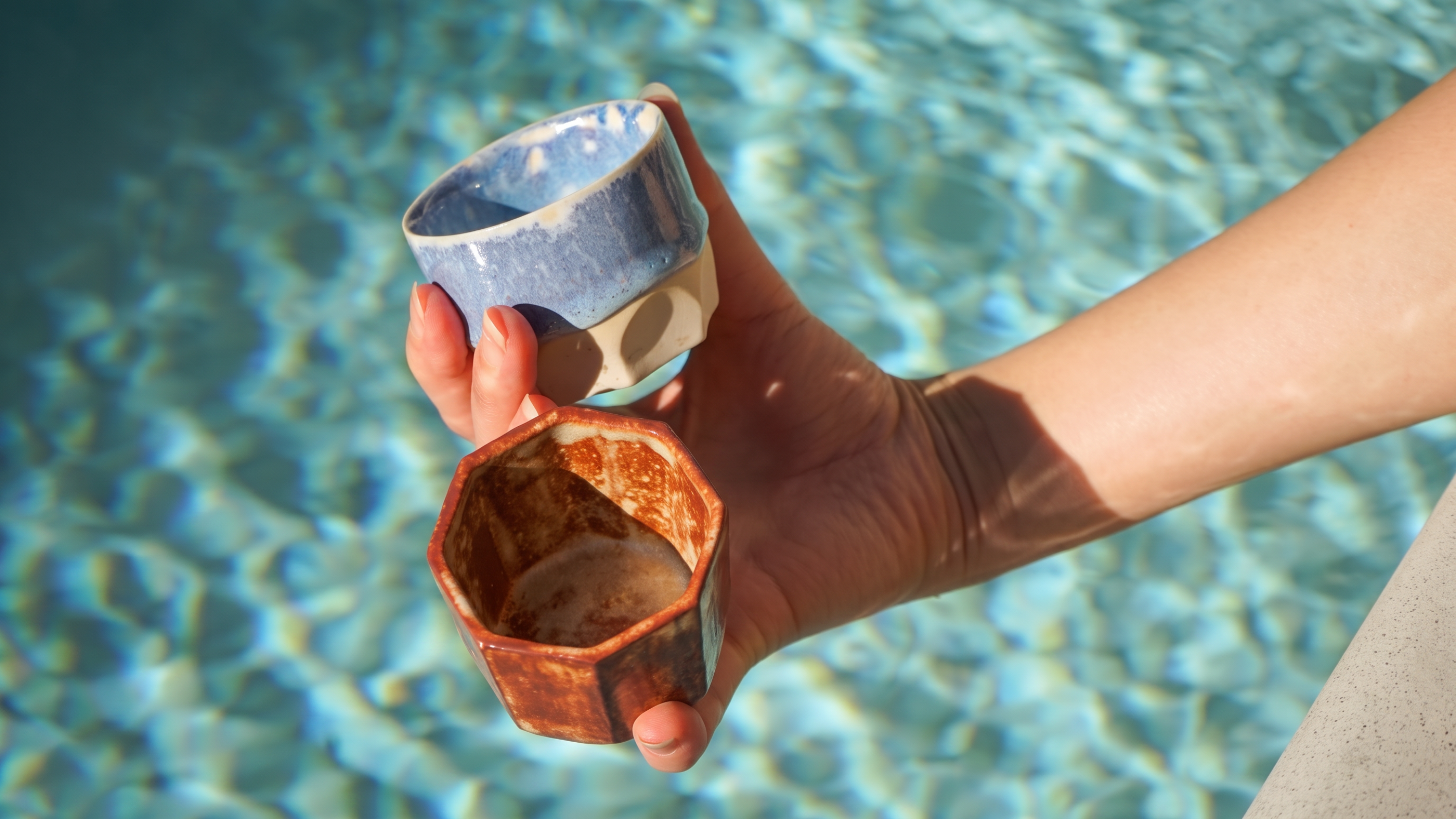 Two glazed tea cups held over swimming pool water