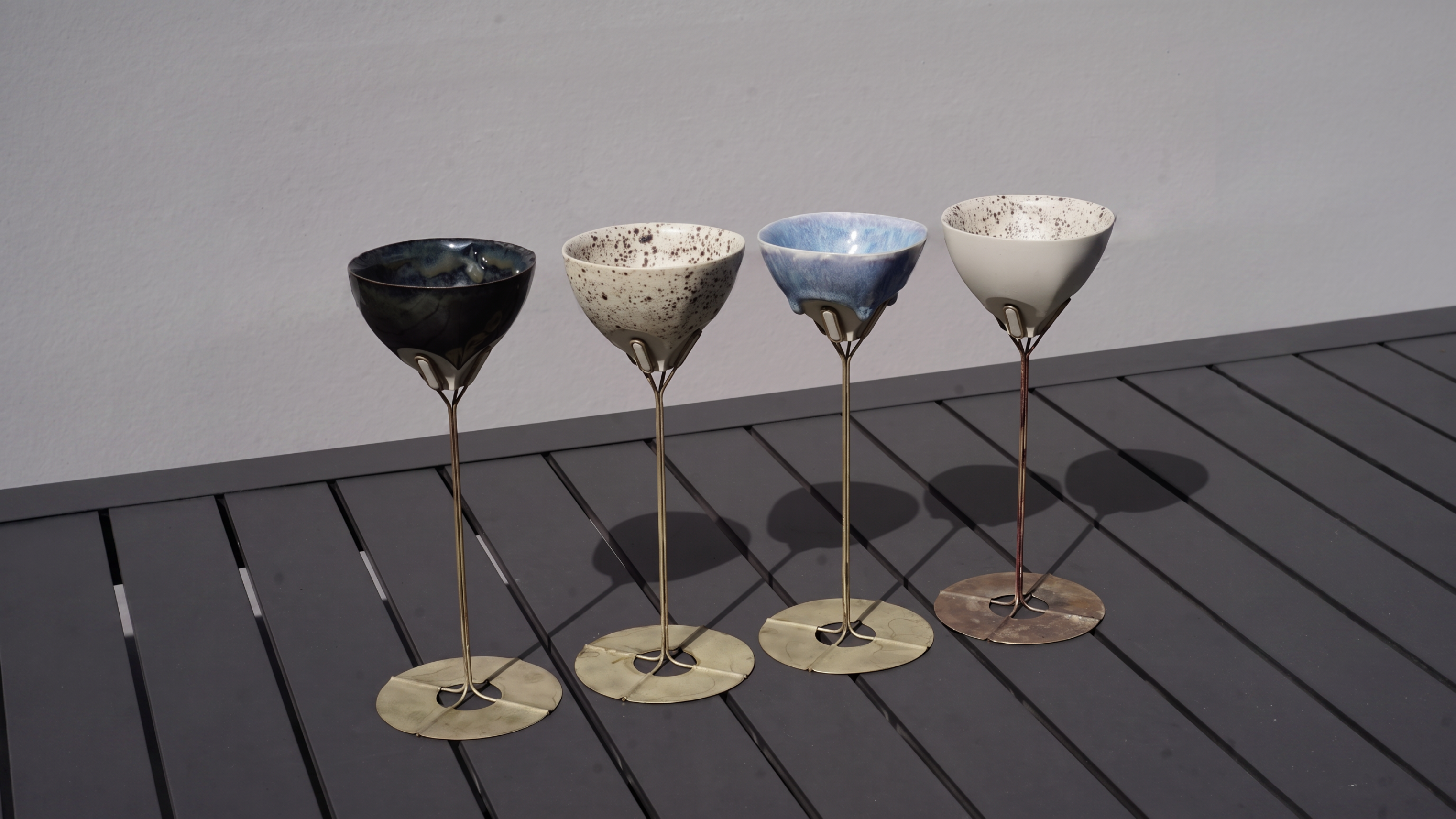 Ceramic cocktail vessels with speckled glaze on a slatted outdoor table